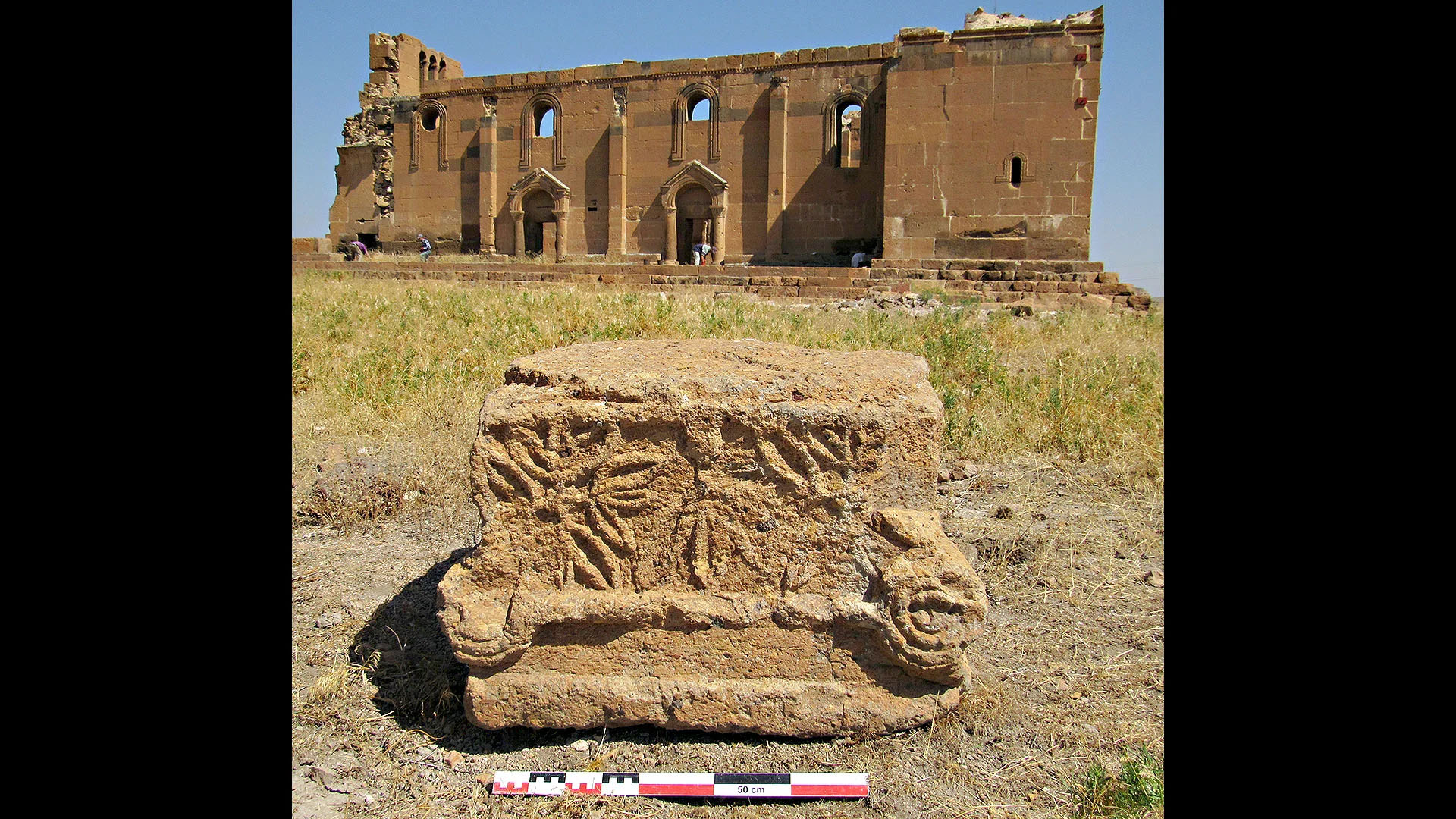 Chapiteau sculpté avec en arrière plan la basilique paléochrétienne 